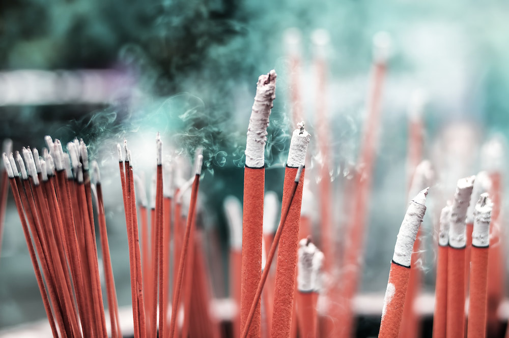 Cluster of bright pink incense sticks with swirling smoke in front go blurry green background