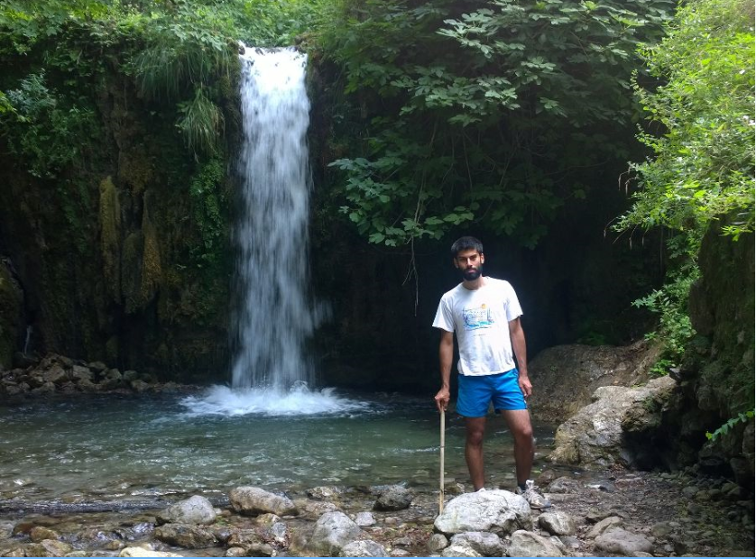 Farshid Soltani standing near the edge of a small pool beneath a water fall