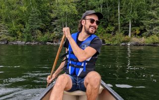 Michael Montess canoeing with a green forest behind him and reflected on the water