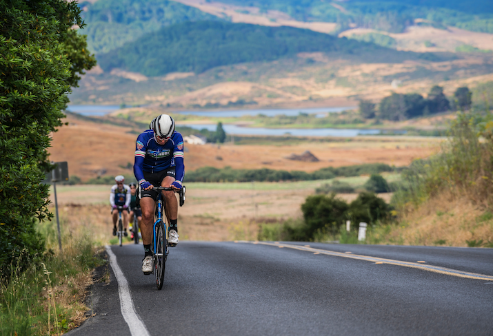 A group of bicyclists ride up a hill on a road through a valley
