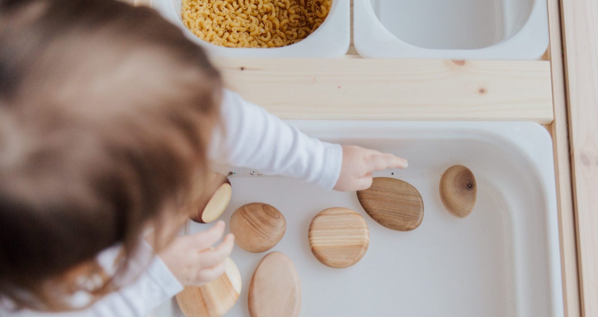 Child exhibits motor development by gathering wooden stones from a tub