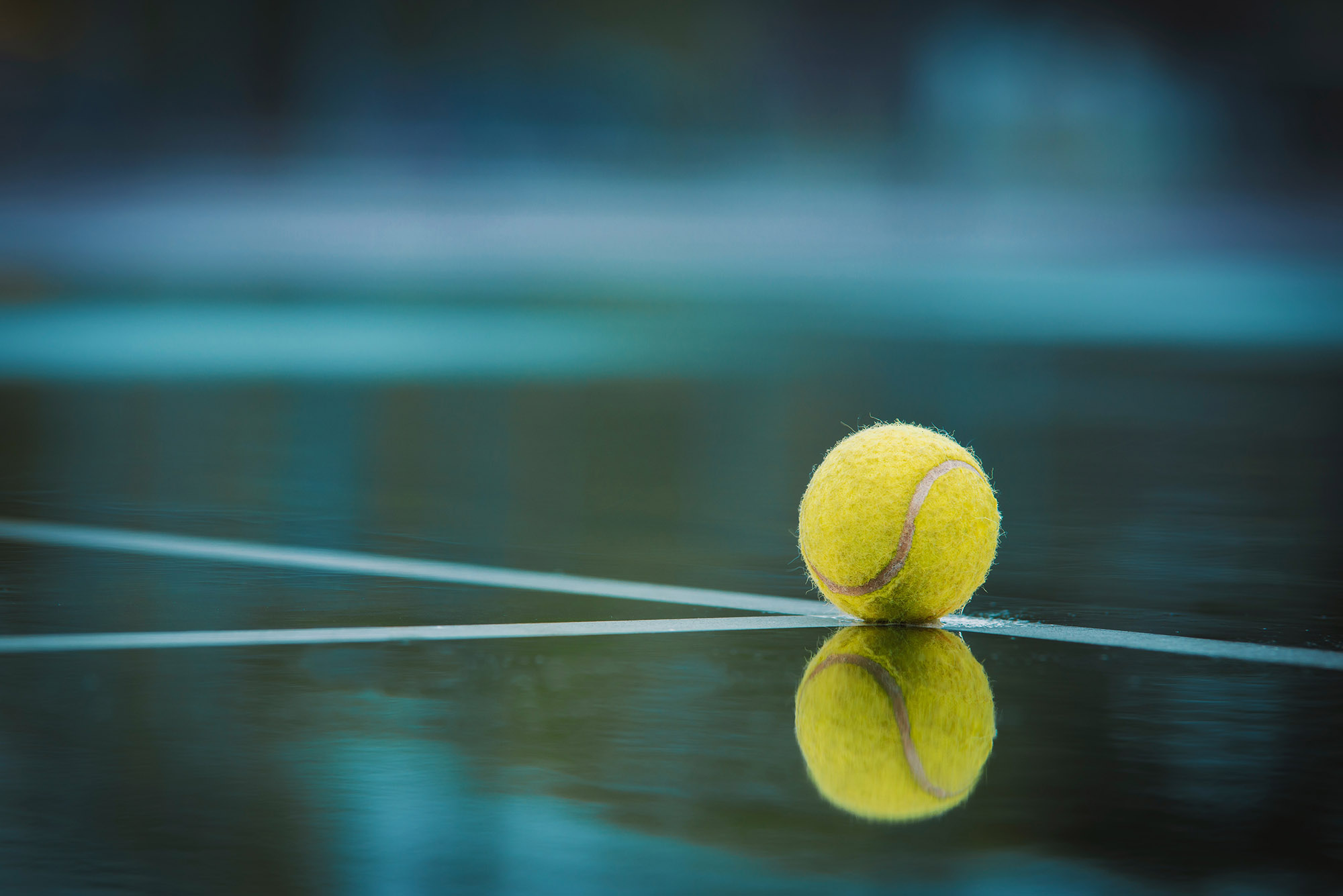 Tennis ball with reflection on surface of tennis court.