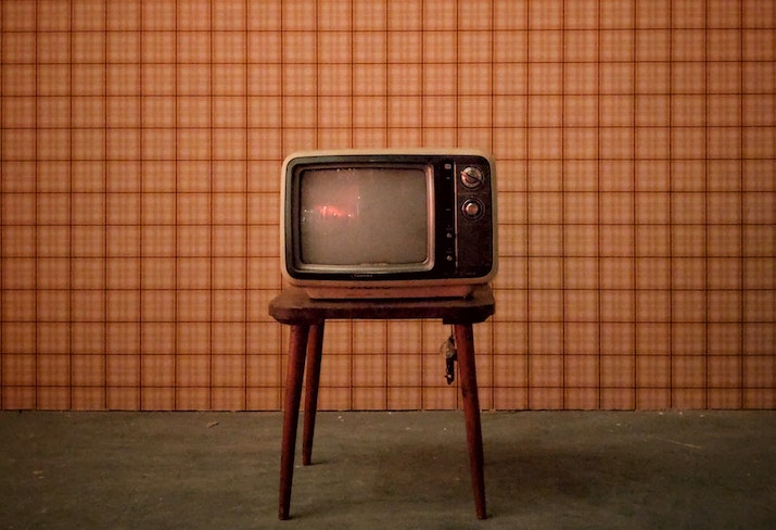 Time and memory event image: an old tv stands on a flat green floor in front of orange plaid wallpaper