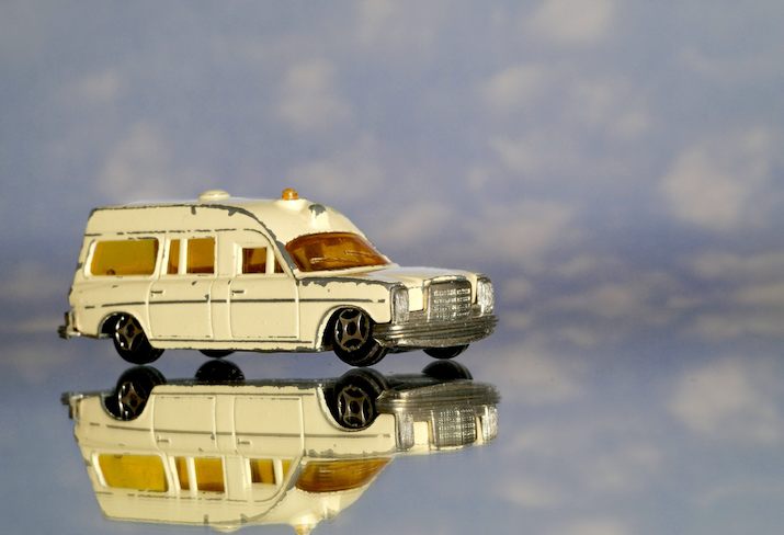 Toy ambulance on a mirror in front of blue sky with clouds; event image for James Wilson, What makes a health system good?